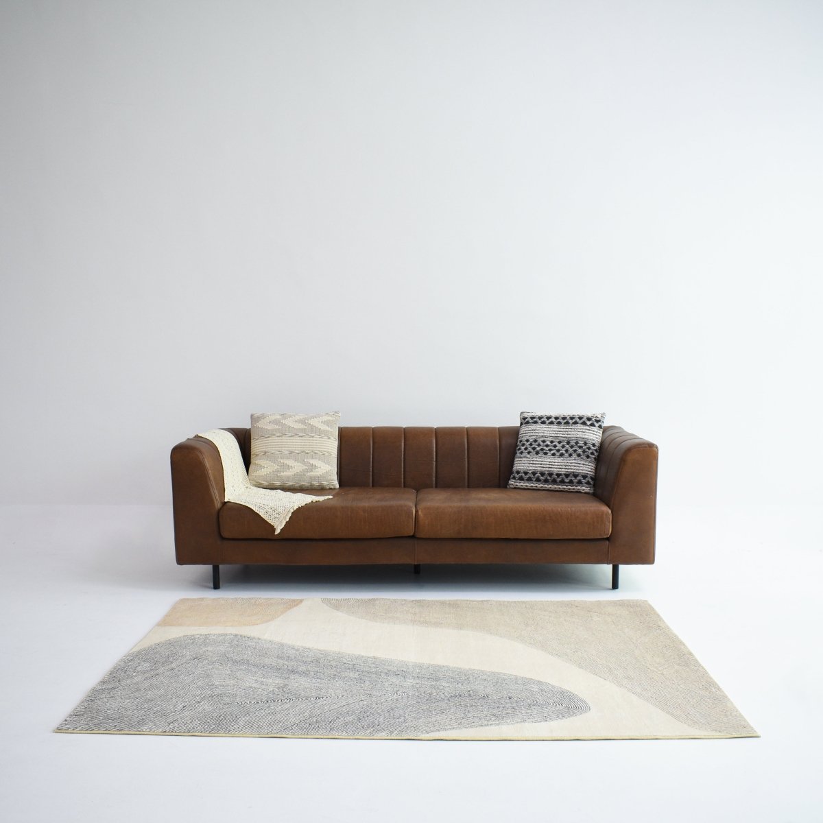 An beige and gray carpet with soft, flowing shapes complements a brown sofa, adding a modern touch to the living space.