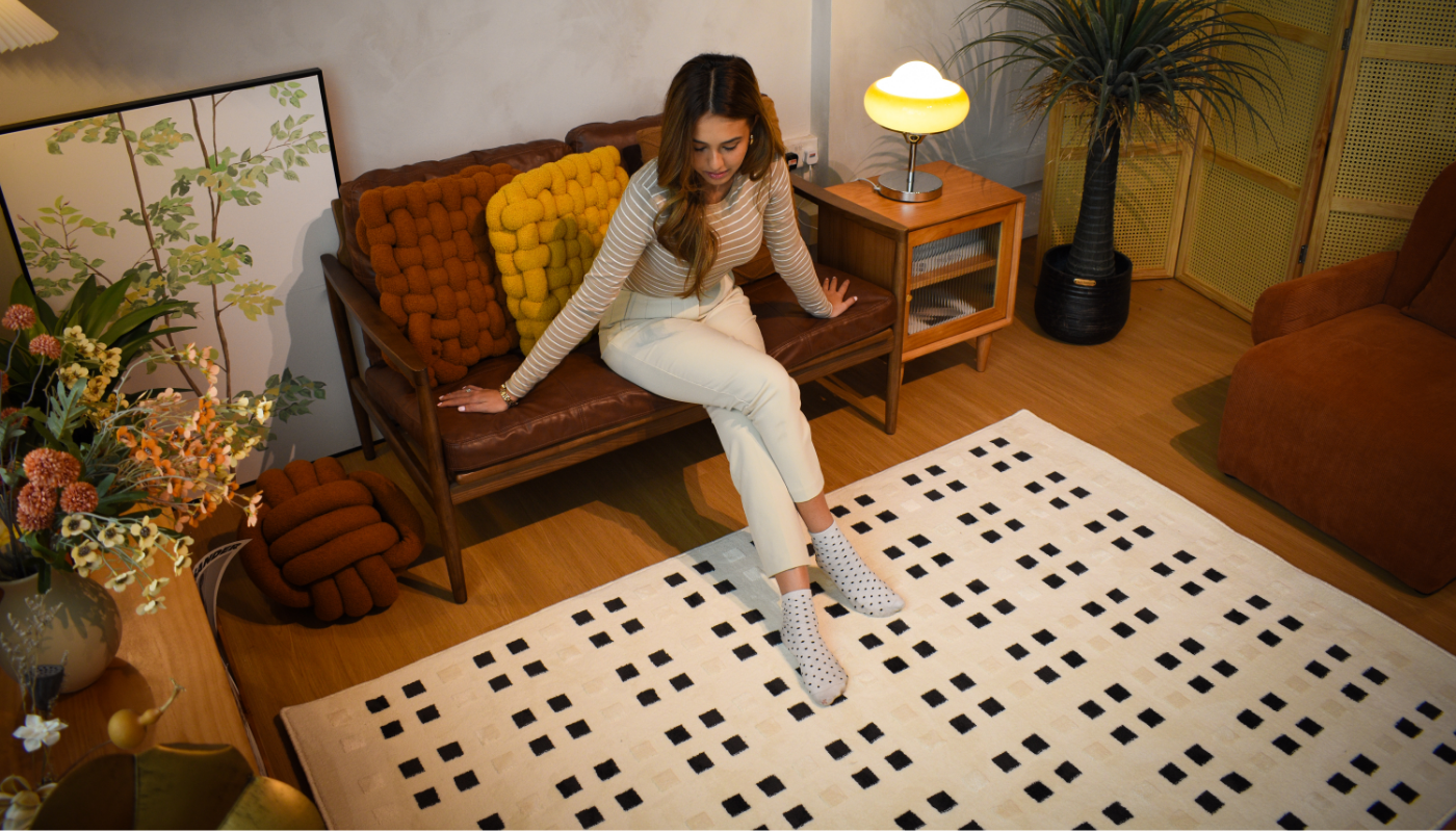 girl stitting on a sofa admiring a cream white carpet with square dots.