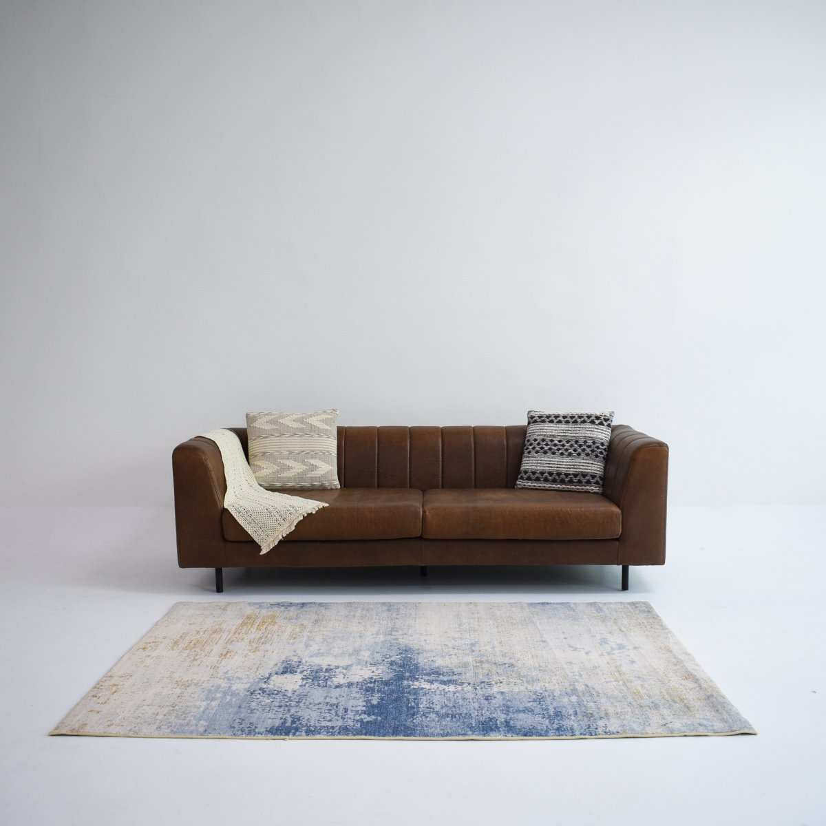 A modern living room featuring a brown sofa, complemented by a blue and beige carpet adding a stylish touch to the space.