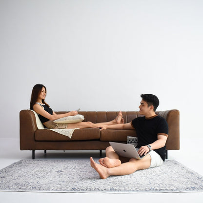 A couple relaxing in a minimalist living room, on a brown sofa. Their feet rest on a blue and white patterned carpet.