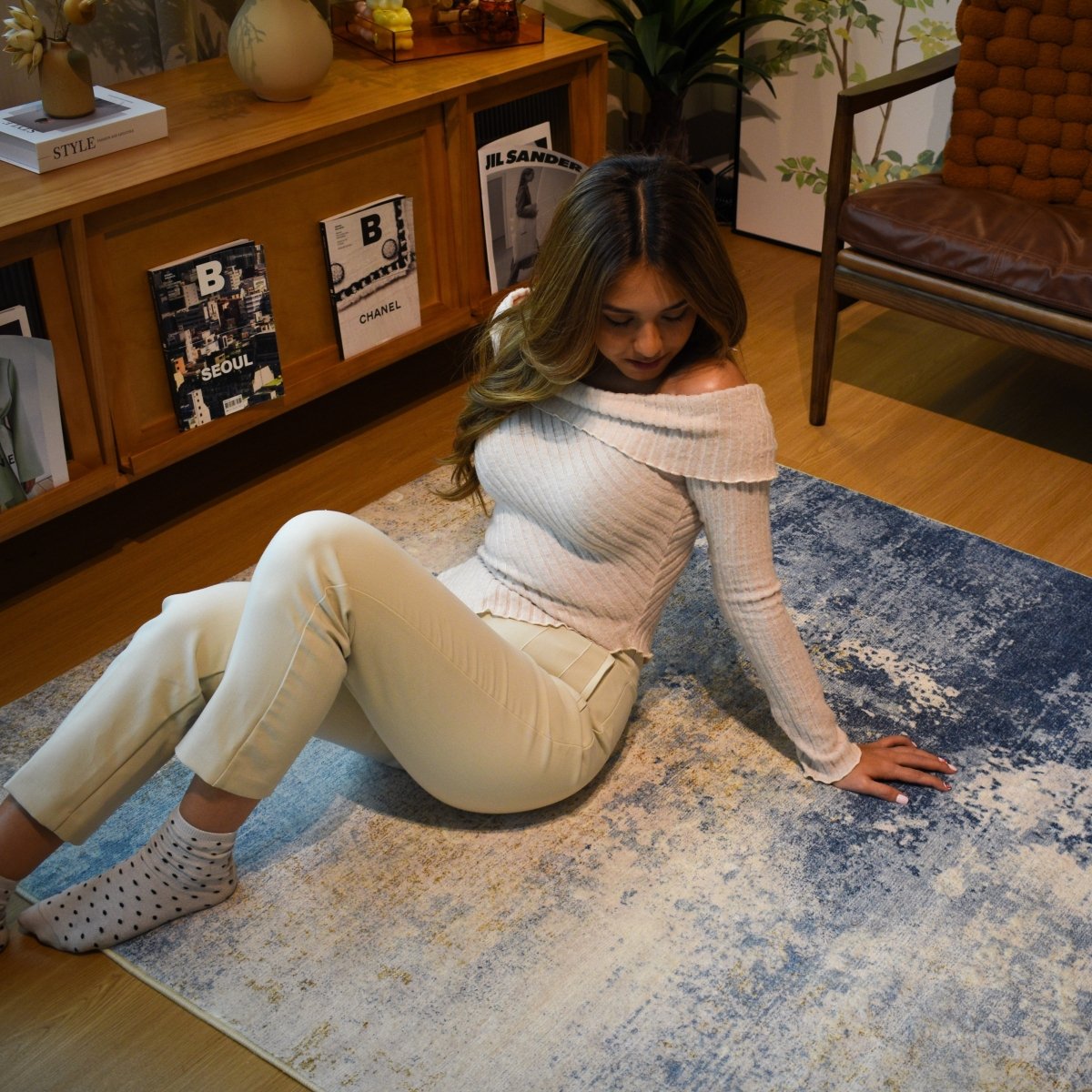 A woman sitting on a beige and blue abstract carpet, adding a modern and cozy touch to the warm-toned living room setting.